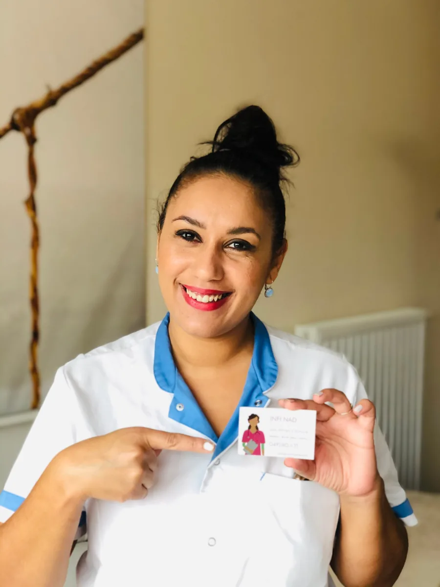 Nadia Cherrak, infirmière, souriante en tenue de soins, montre sa carte INFI NAD